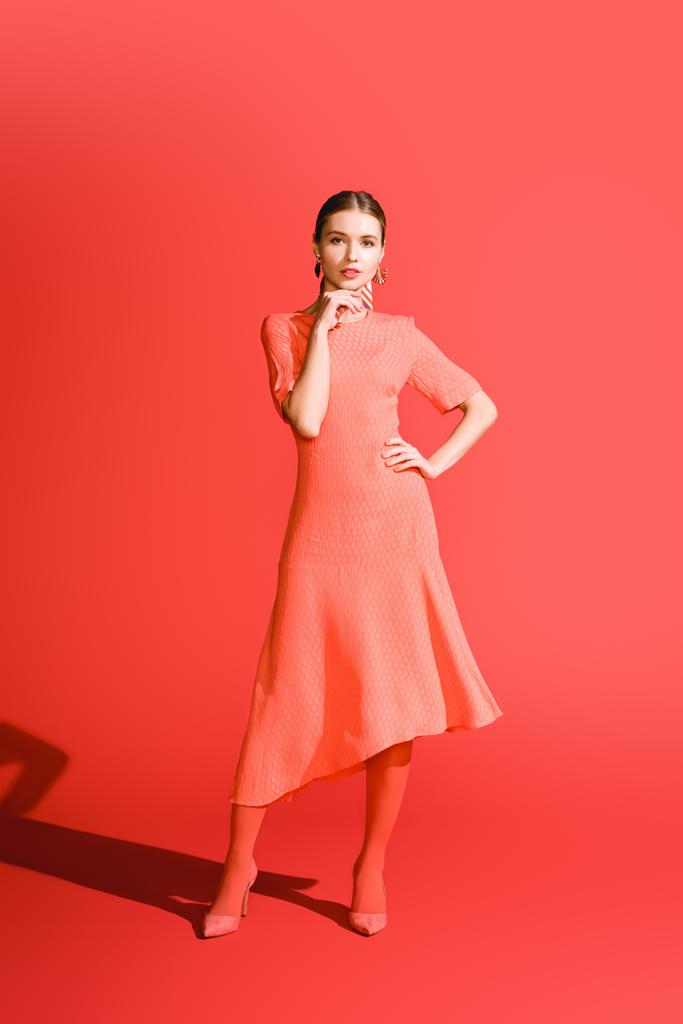 mujer joven con estilo posando en vestido de coral vivo sobre fondo rojo
 - Foto, Imagen