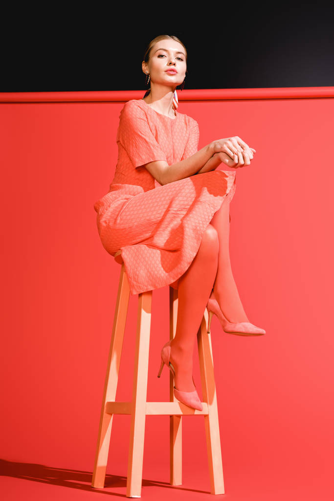 divat lő modell jelentő élő korall ruha piros háttérben a széken - Fotó, kép