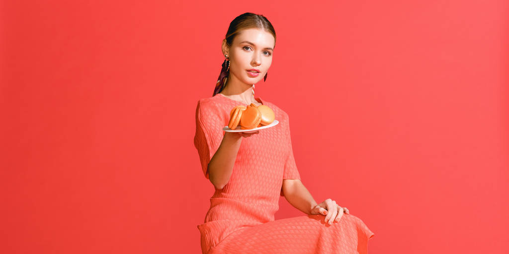 attractive girl holding plate with macaroons isolated on living coral. Pantone color of the year 2019 concept - Photo, Image