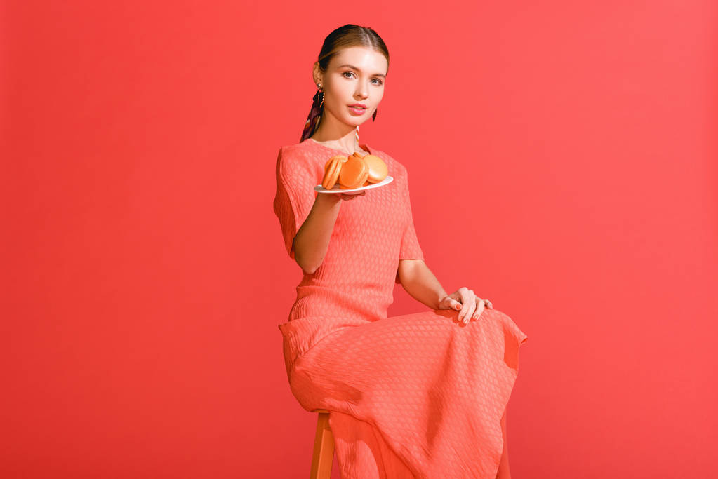 bella donna in possesso di piatto con amaretti isolati su corallo vivo. Pantone colore dell'anno 2019 concept
 - Foto, immagini
