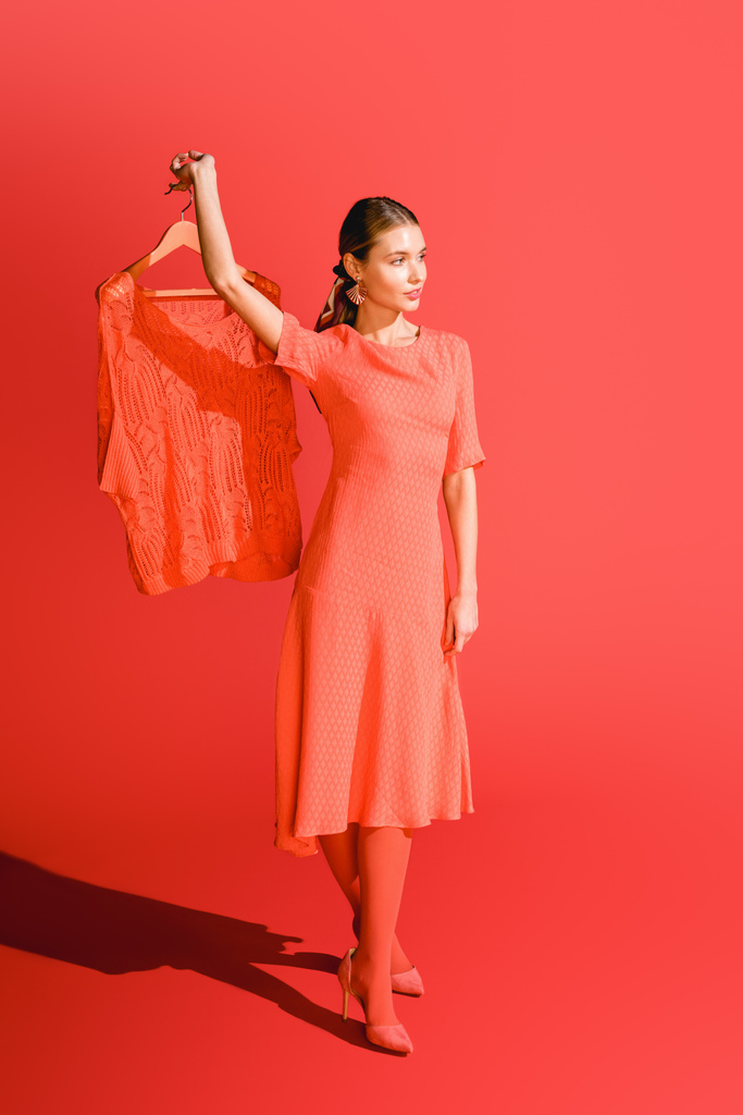модна жінка тримає вішалку з одягом на живому коралі. Концепція кольору пантона 2019 року
 - Фото, зображення