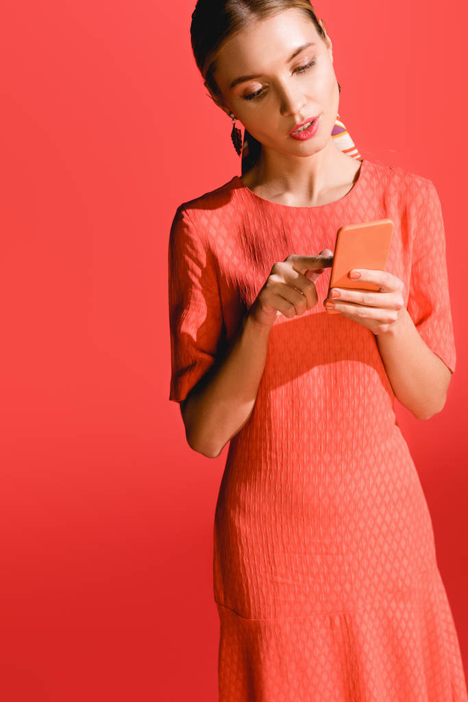 ελκυστική γυναίκα σε ζουν κοραλλιών φόρεμα χρησιμοποιώντας το smartphone στο κόκκινο. Pantone χρώμα της έννοιας έτος 2019 - Φωτογραφία, εικόνα
