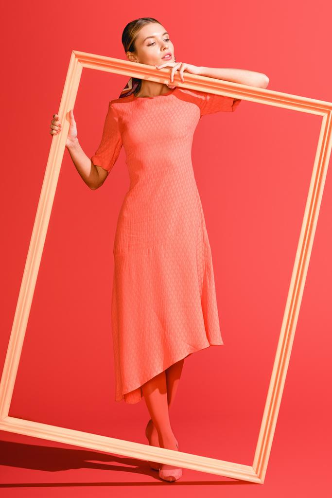 fashionable elegant woman in dress posing with big frame on living coral. Pantone color of the year 2019 concept - Photo, Image