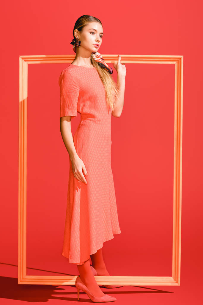 trendy jonge vrouw in trendy jurk poseren met grote frame op levende koraal. PANTONE-kleur van het jaar 2019-concept - Foto, afbeelding