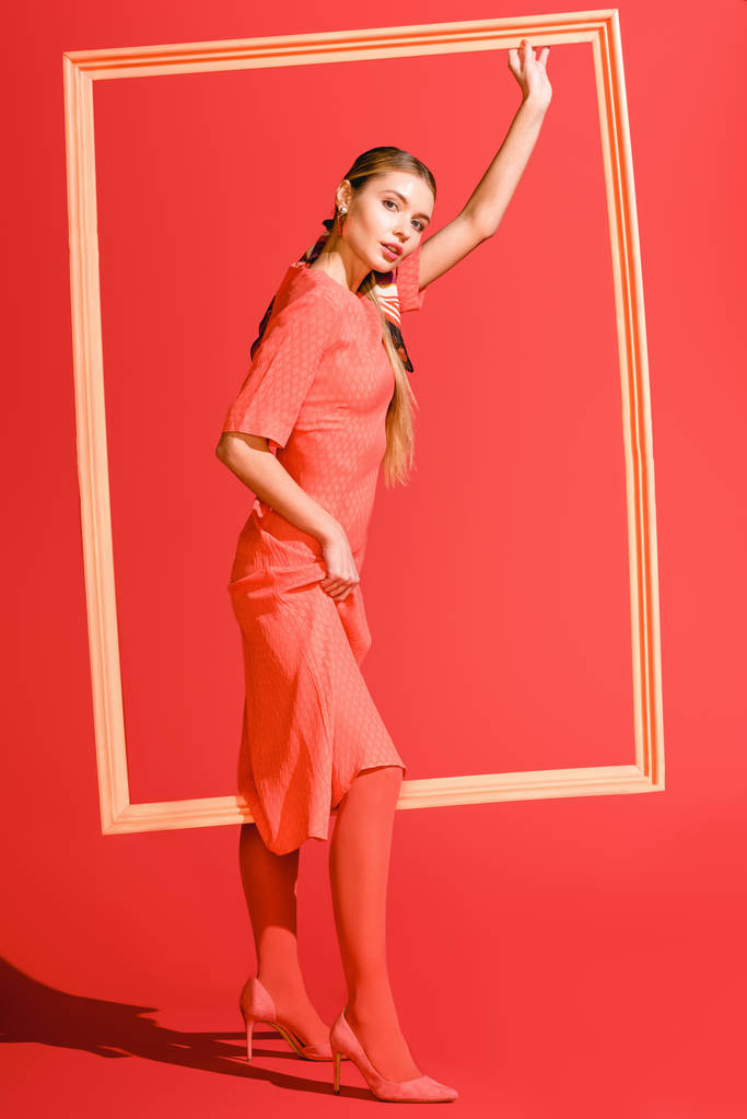 mode-shoot met stijlvolle model in jurk poseren met grote frame op levende koraal. PANTONE-kleur van het jaar 2019-concept - Foto, afbeelding