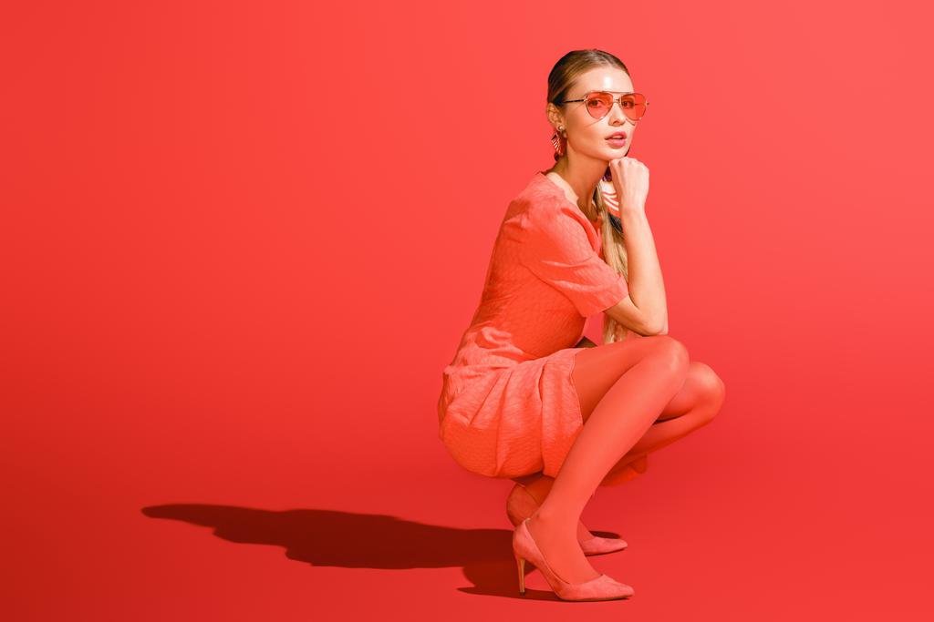 stílusos modellt jelentő élő coral ruha és piros háttéren napszemüveg - Fotó, kép