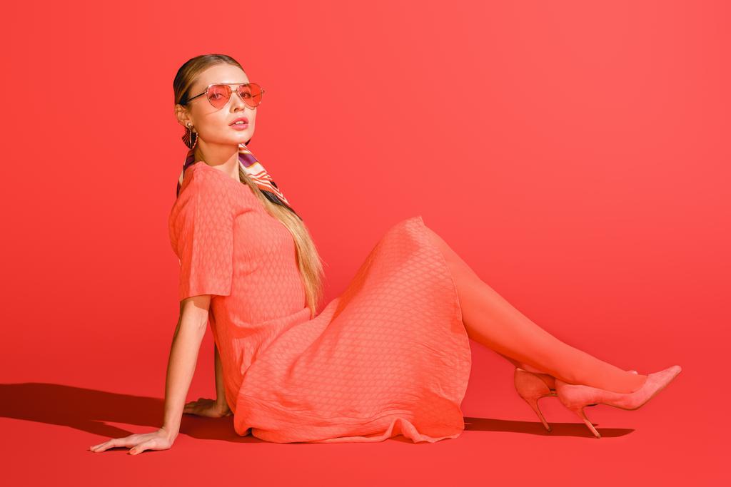 модная модель в живом коралловом платье и солнцезащитных очках на красном фоне
 - Фото, изображение