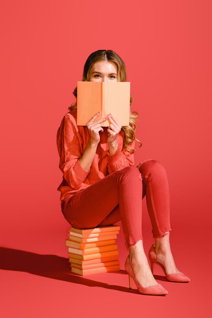 fashionable girl reading book while sitting on books on living coral. Pantone color of the year 2019 concept - Photo, Image