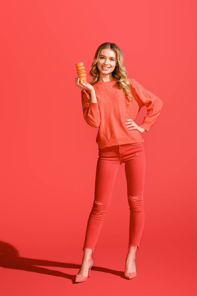 cheerful woman holding sweet macaroons on living coral. Pantone color of the year 2019 concept - Photo, Image