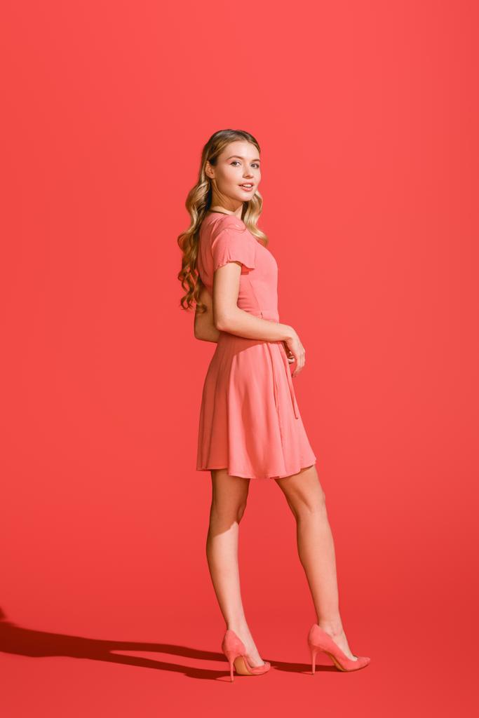 stijlvolle blond meisje poseren in levende koraal jurk op rode achtergrond - Foto, afbeelding