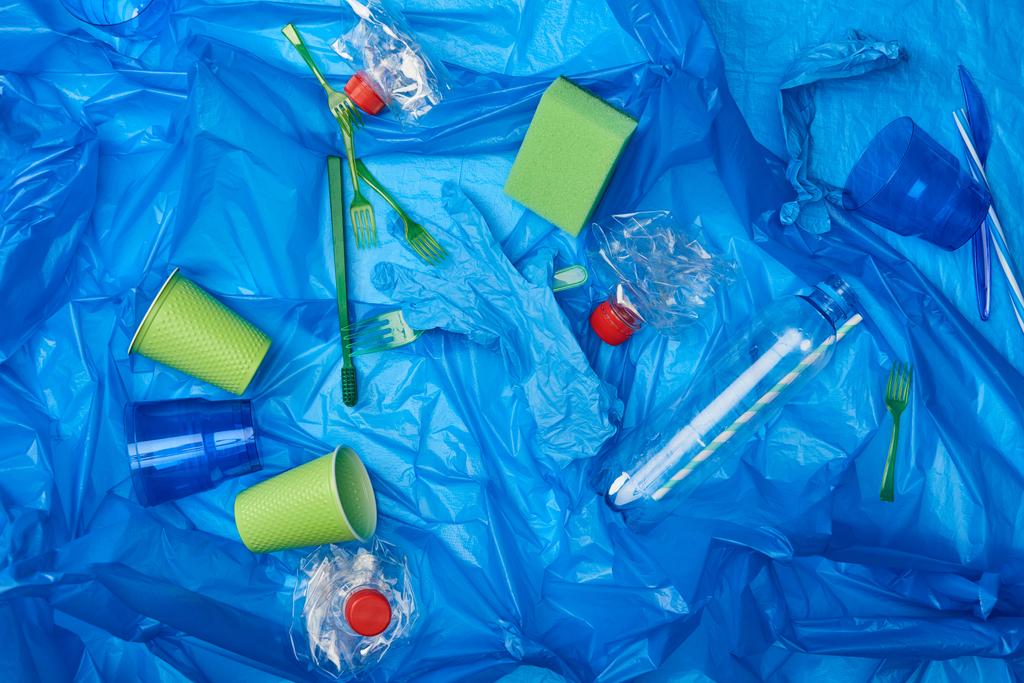 bovenaanzicht van blauwe verfrommeld polyethyleen zak met plastic flessen, wegwerp servies ang spons - Foto, afbeelding