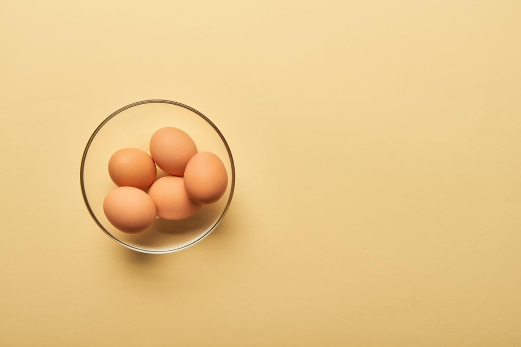 bovenaanzicht van verse eieren in glazen kom op gele achtergrond - Foto, afbeelding