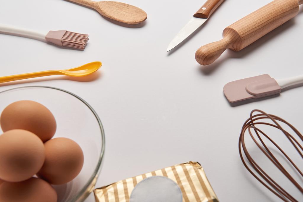 utensilios de cocina, mantequilla y huevos en un tazón sobre una superficie gris
 - Foto, Imagen