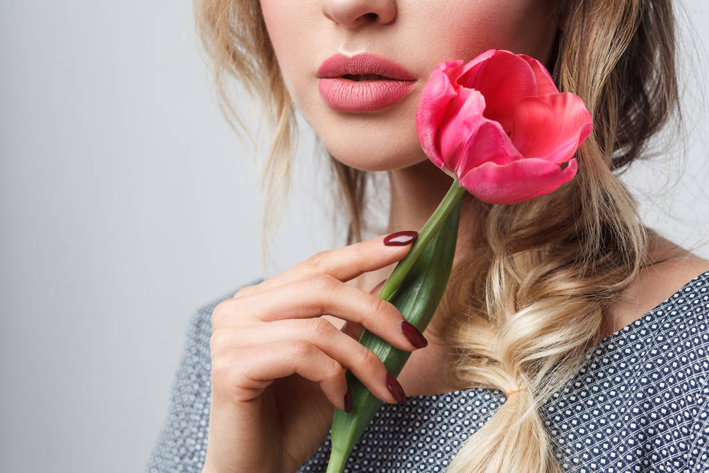 attraktives Modemodel mit sinnlichen Lippen, die Tulpe mit Zärtlichkeit in ihrer schönen Hand haltend  - Foto, Bild