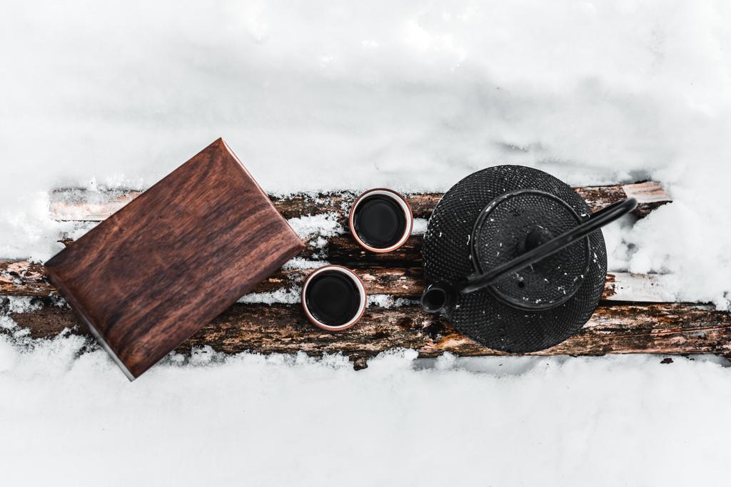 top view of kettle, cups with tea and wooden box on logs among snow - Photo, Image