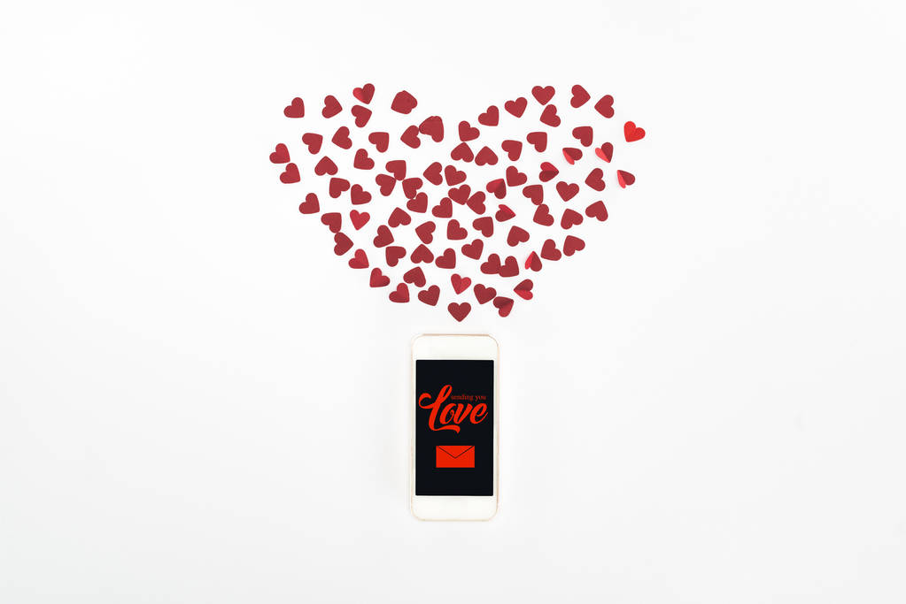 Flat lay with red heart symbols and smartphone with "sending you love" lettering isolated on white, st valentine day concept - Photo, Image