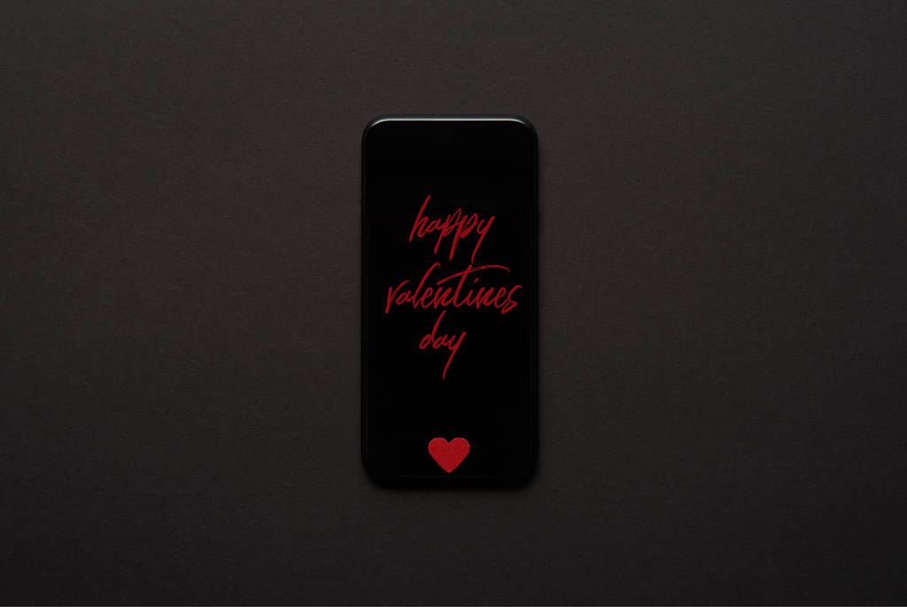 κάτοψη του smartphone με επιγραφή «Ευτυχισμένη ημέρα του Αγίου Βαλεντίνου» και μικρή κόκκινη καρδιά συνδεθείτε σε σκούρο φόντο - Φωτογραφία, εικόνα