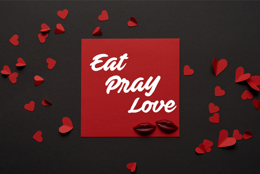 vue du haut du carton rouge avec lettrage "manger, prier, aimer" et lèvres en chocolat et coeurs coupés en papier
  - Photo, image