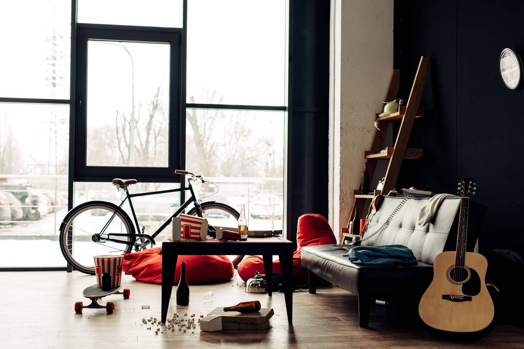 salontafel met eten en drinken in de buurt van Bank en akoestische gitaar in rommelige woonkamer - Foto, afbeelding