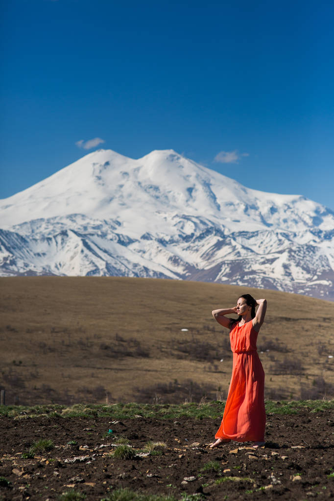 Porträt einer Frau in einem langen roten Kleid vor dem Hintergrund eines hohen schneebedeckten Berges - Foto, Bild