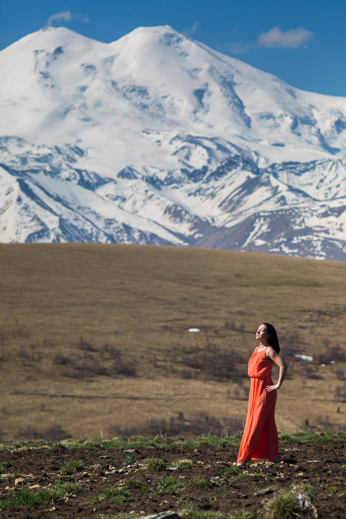 brünette Frau im langen roten Kleid vor dem Hintergrund hoher schneebedeckter Berge  - Foto, Bild