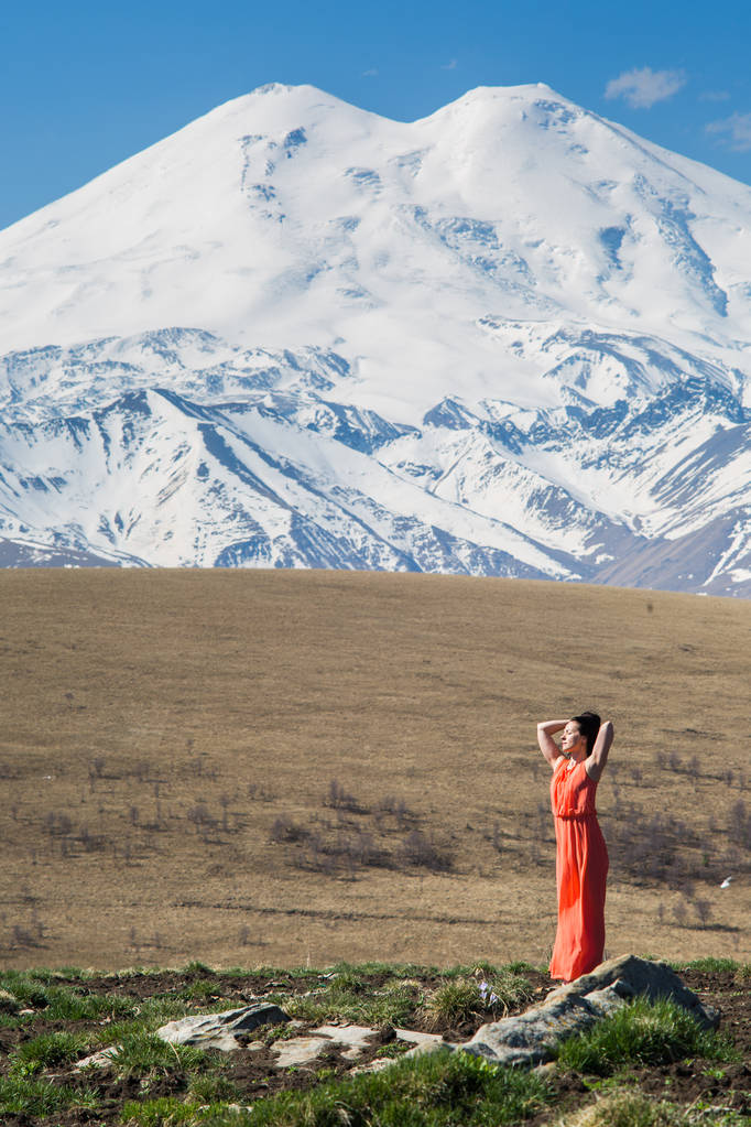 Porträt eines vollwertigen Mädchens in einem roten Kleid vor dem Hintergrund hoher schneebedeckter Berge - Foto, Bild