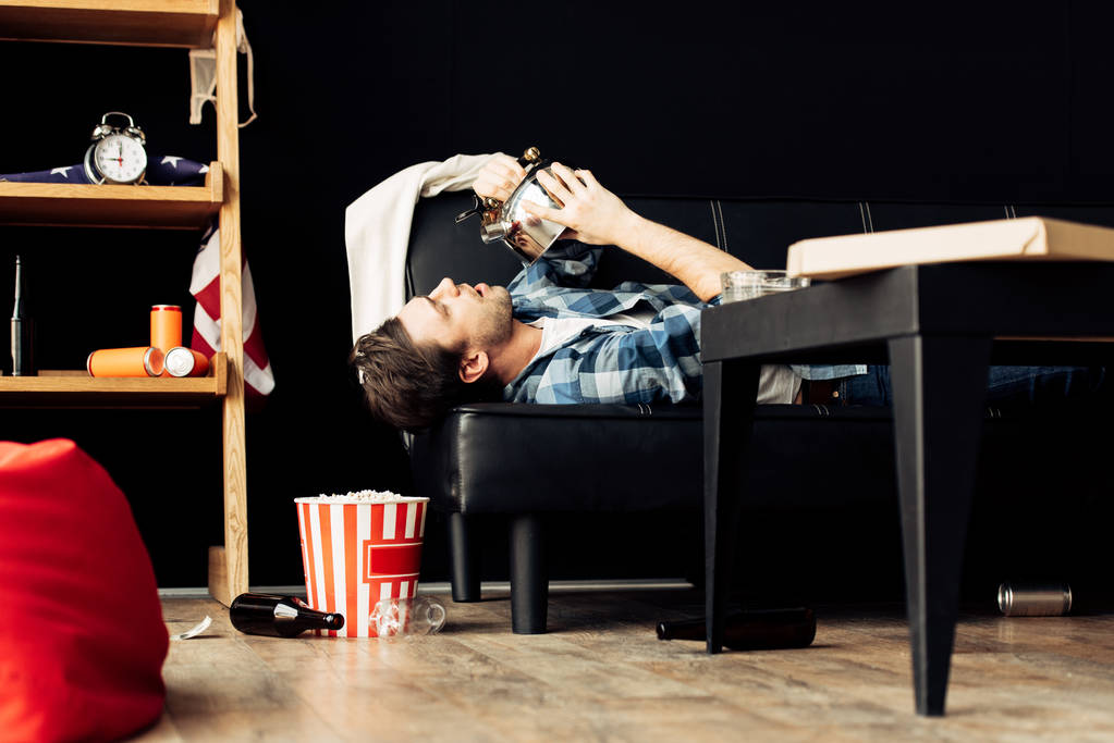 ティーポットから乱雑なリビング ルームでソファの上に横たわっている間飲む男性  - 写真・画像