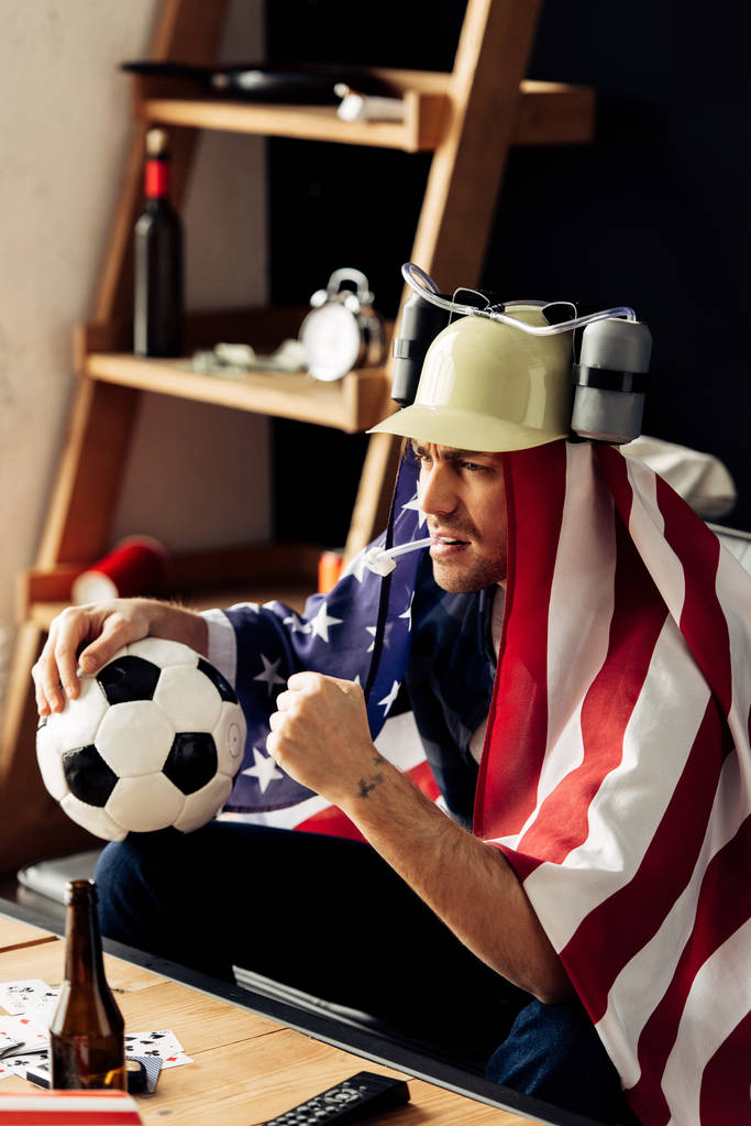 Mann mit Bierhelm beobachtet Spiel mit amerikanischer Flagge auf Schultern - Foto, Bild