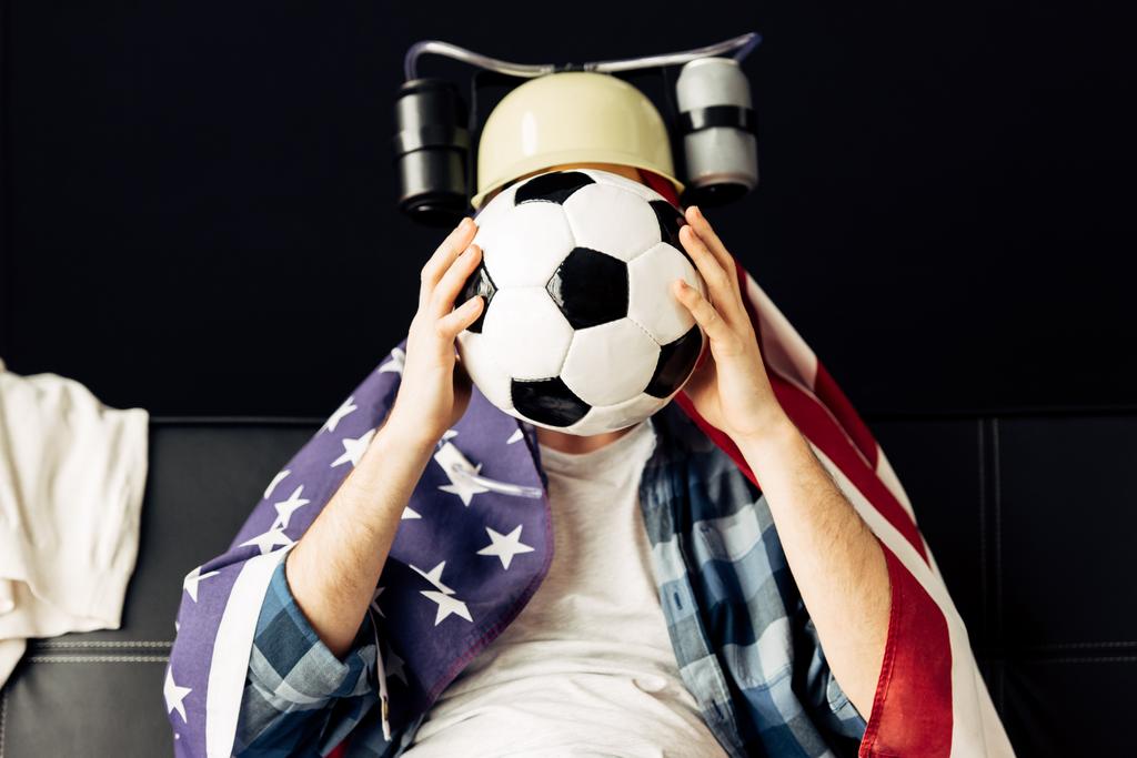 man dragen bier helm die betrekking hebben op gezicht met voetbal en zit met de Amerikaanse vlag op de schouders - Foto, afbeelding