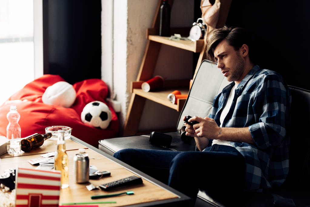 hombre cansado jugando videojuego en la sala de estar desordenada
 - Foto, imagen
