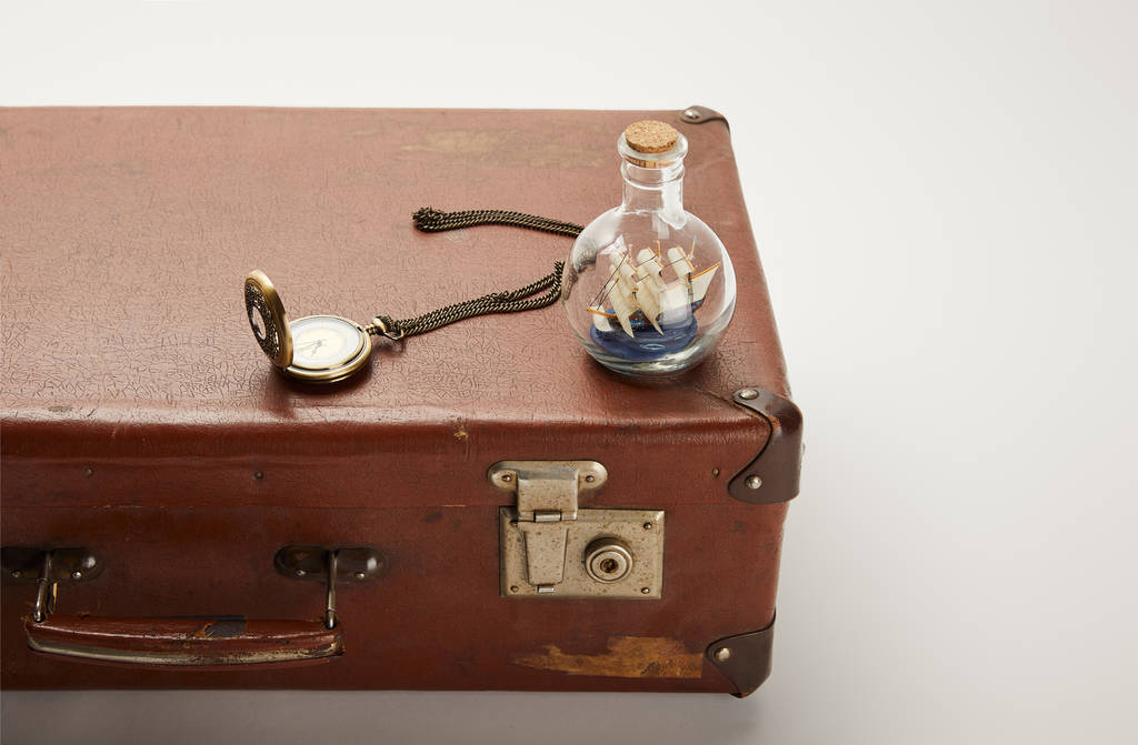 speelgoed schip in glazen fles en kompas op bruine koffer met kopie ruimte  - Foto, afbeelding