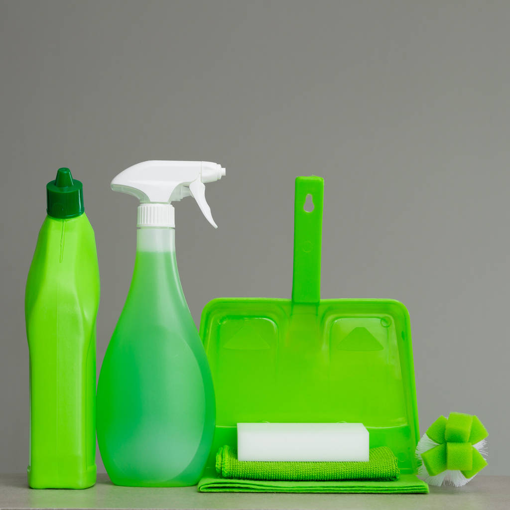 Zelená láhev pracího prostředku na WC, láhev s rozprašovačem, kartáč, houba, lopatka a prach na šedém pozadí. Čištění nástroje. - Fotografie, Obrázek