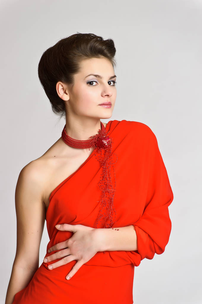 schöne junge Brünette in rot mit einer Halskette um den Hals auf weißem Studiohintergrund - Foto, Bild