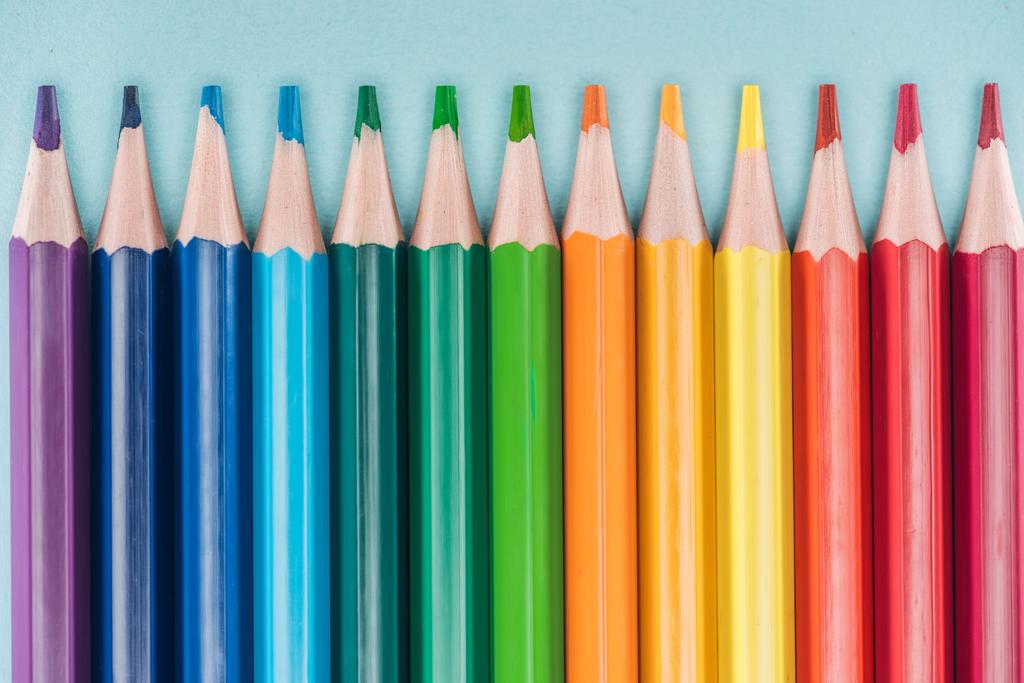 top view of rainbow multicolored pencils arranged in horizontal line on blue background, lgbt concept - Photo, Image