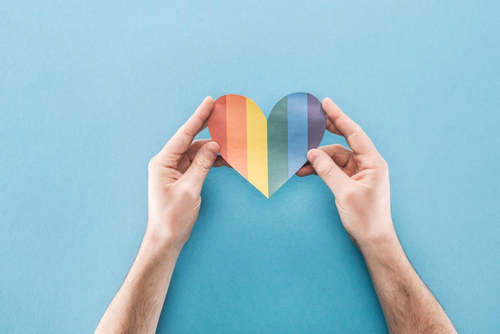 vista recortada de manos masculinas con corazón de papel de color arco iris sobre fondo azul, concepto lgbt
 - Foto, imagen