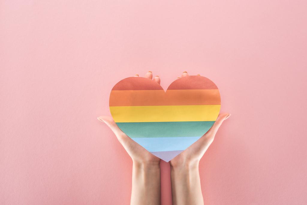 vista parcial de la mujer sosteniendo el corazón de papel de color arco iris sobre fondo rosa, concepto lgbt
 - Foto, imagen