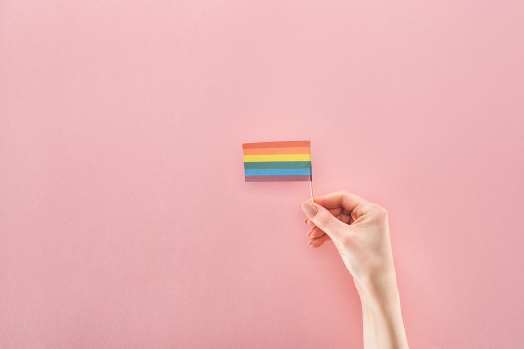 μερική άποψη του γυναικείου χεριού με σημαία ουράνιο τόξο χαρτί σε ροζ φόντο, ΛΟΑΤ έννοια - Φωτογραφία, εικόνα