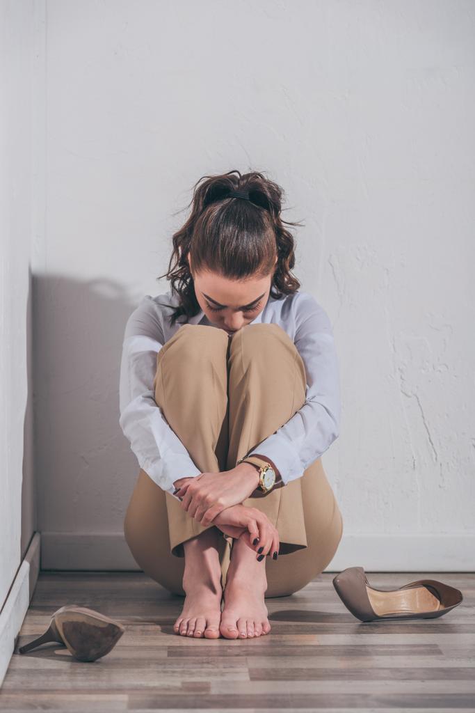smutna Kobieta w białej bluzce i beż spodnie, siedząc na podłodze, tulenie kolana blisko ściany w domu, żałoby koncepcja zaburzenia - Zdjęcie, obraz