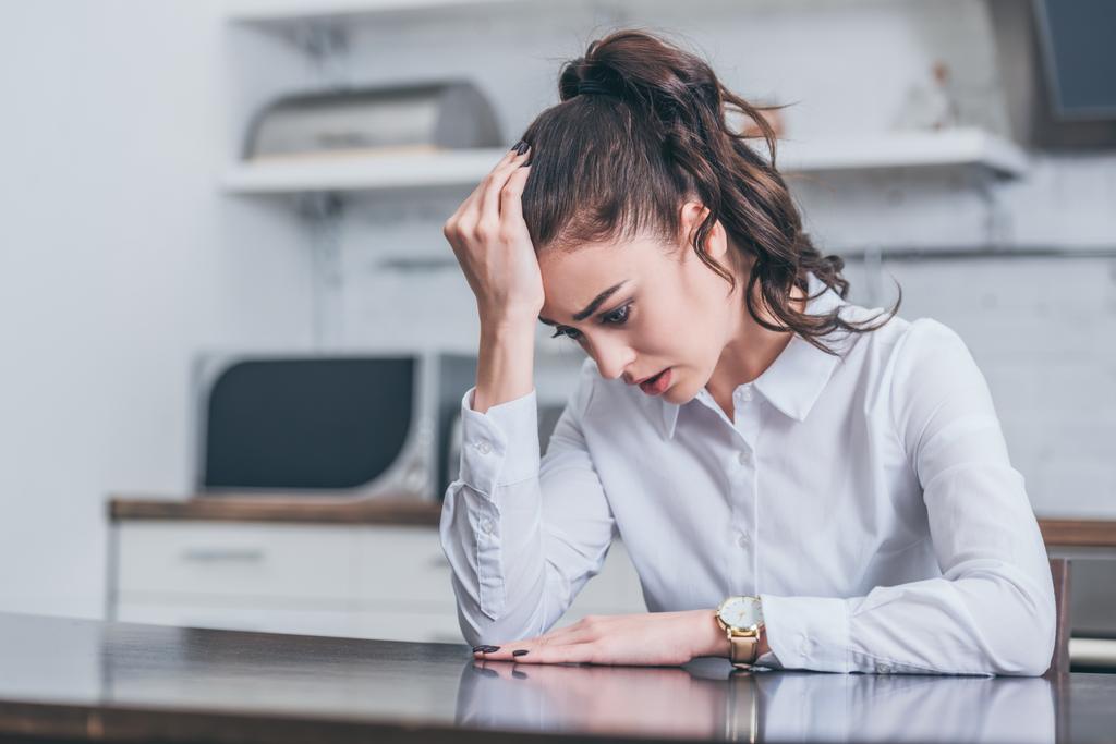 upset woman in white blouse sitting at table and crying in kitchen, grieving disorder concept - Photo, Image