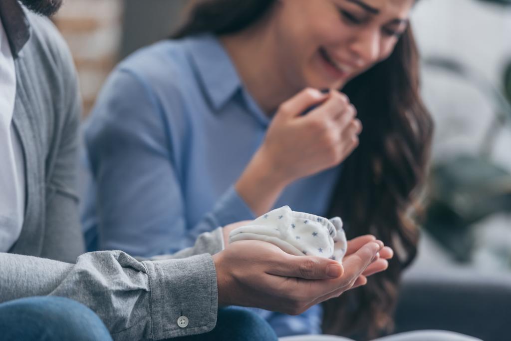 cropped view of man holding baby socks while woman crying at home, grieving disorder concept - Photo, Image