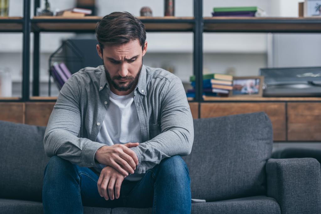 depressed man sitting and grieving on couch in living room - Photo, Image