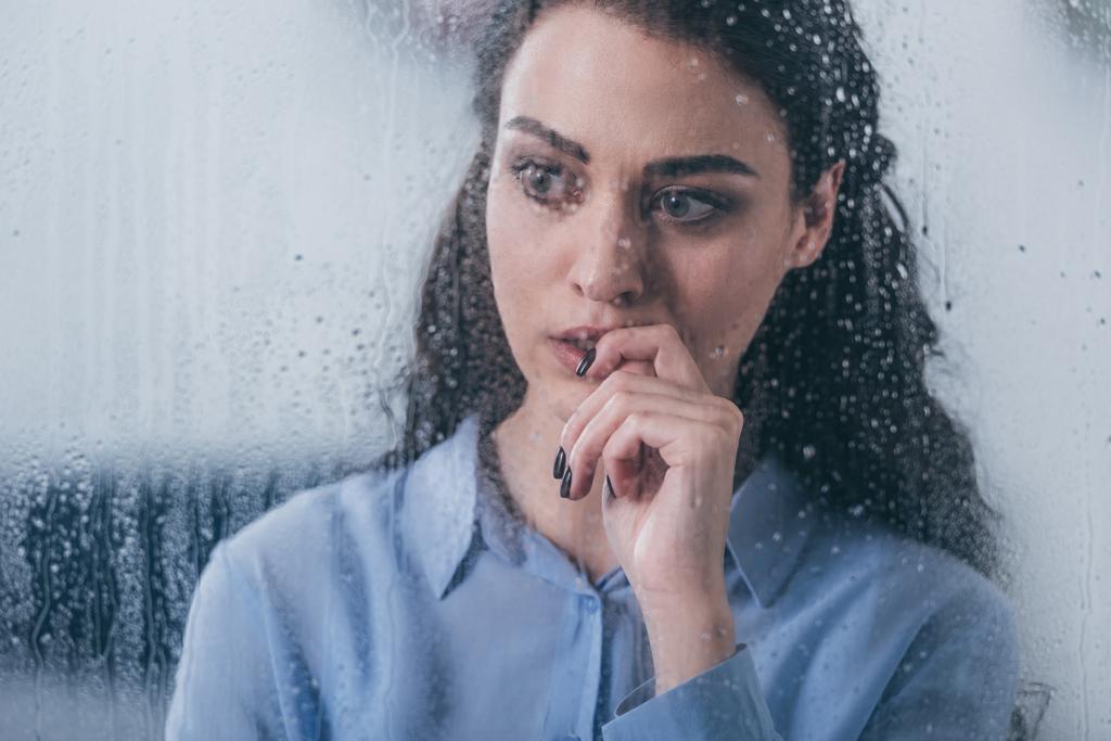 красивая расстроенная женщина трогает лицо и смотрит в окно с капельками дождя
 - Фото, изображение