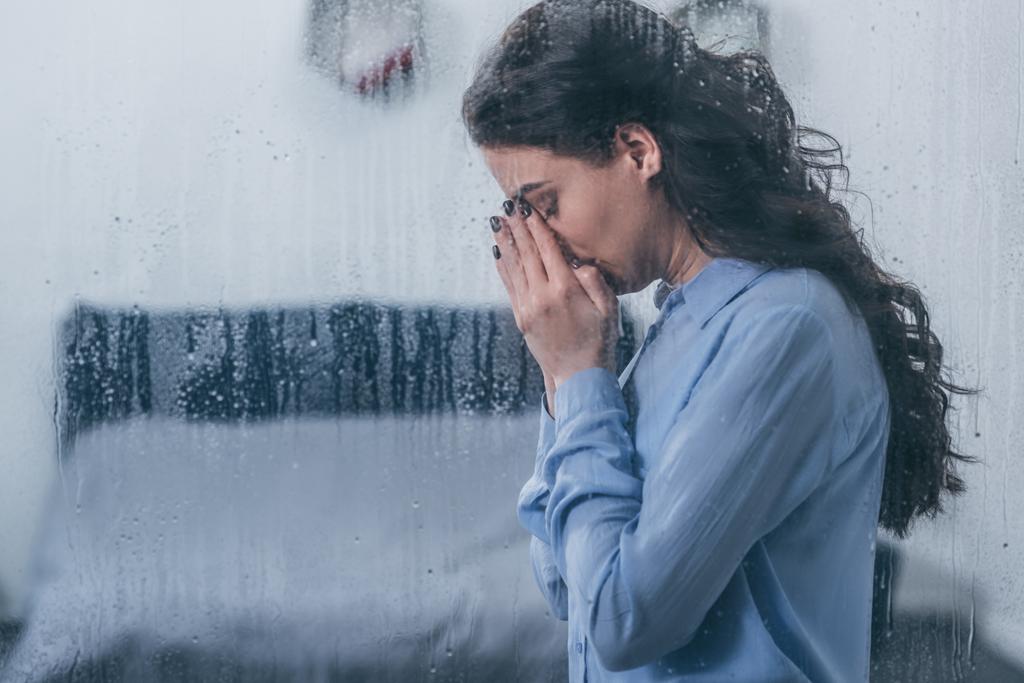 yüzünü elleriyle kapsayan ve yağmur damlaları ve kopya alanı ile pencereden evde ağlıyor depresif kadın - Fotoğraf, Görsel