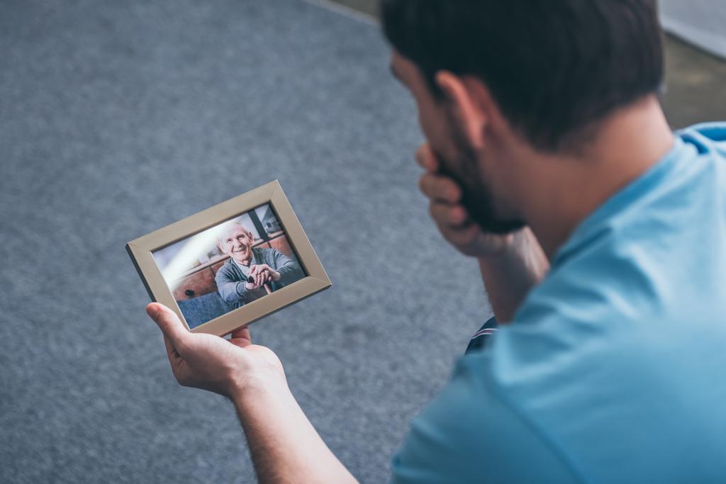 成人男性の老人を自宅でフォト フレームを見ながら悲嘆の背面図 - 写真・画像