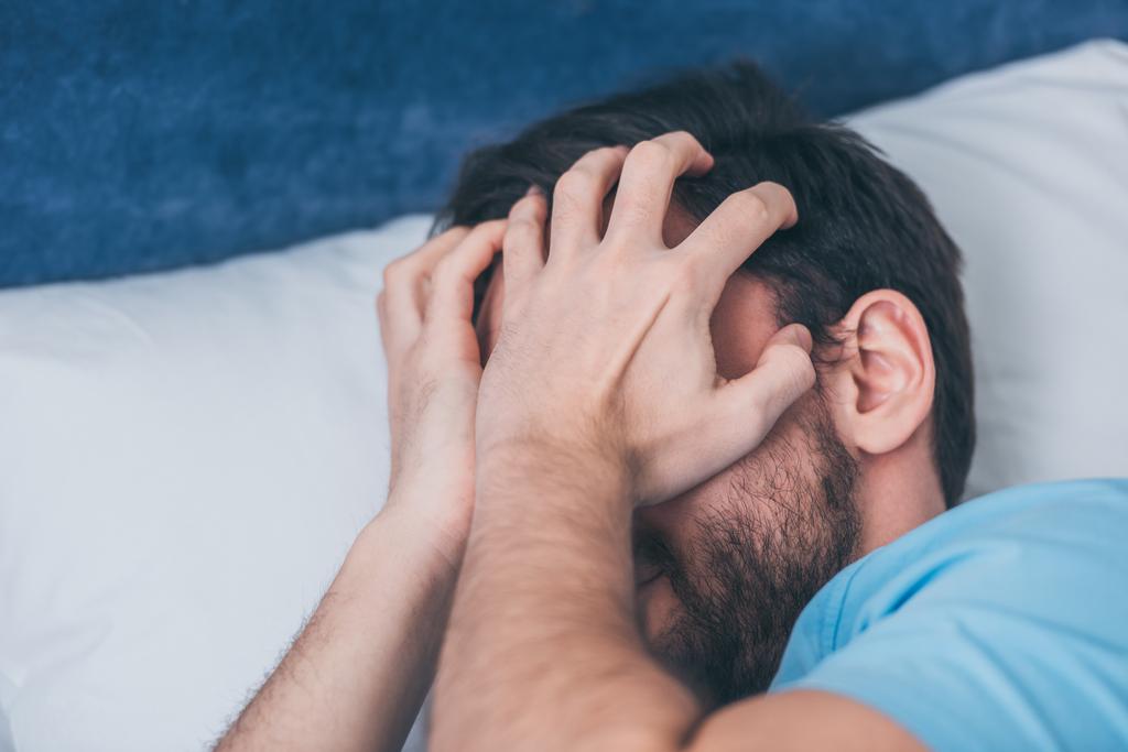 rouwende man in bed liggen, die betrekking hebben op gezicht met handen en huilen thuis - Foto, afbeelding