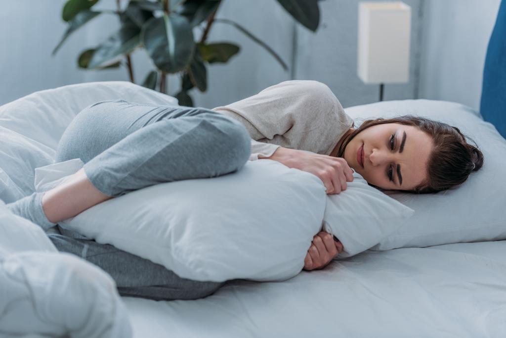 枕を押しながら自宅のベッドで横になっているパジャマを着て悲しい女性の選択と集中 - 写真・画像