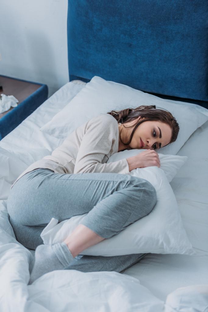 mujer triste en pijama sosteniendo almohada y acostada en la cama en casa
 - Foto, Imagen