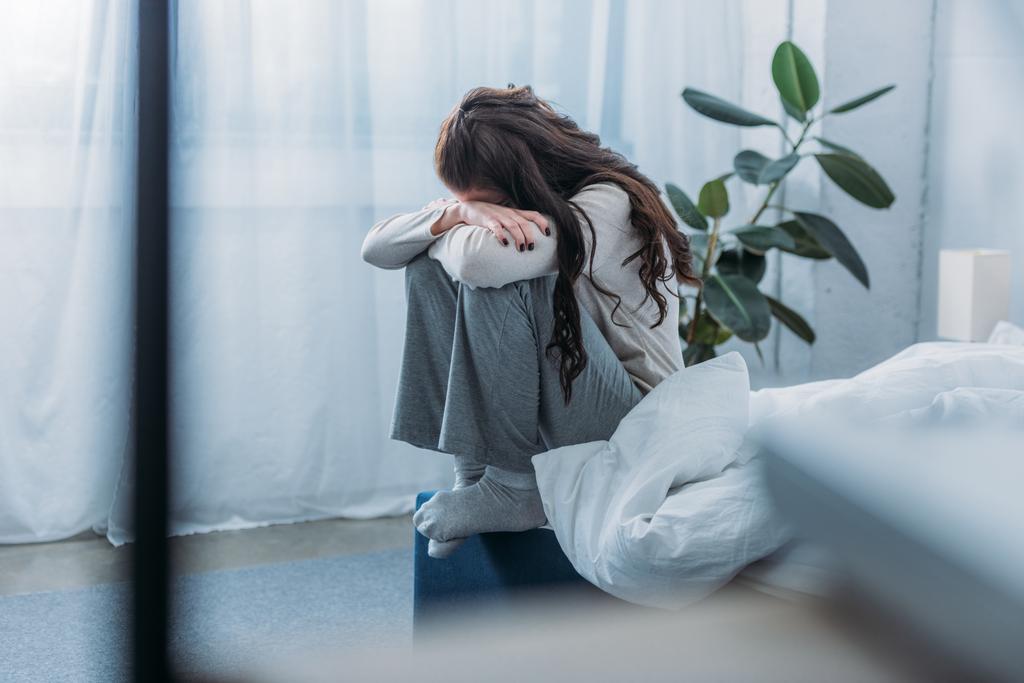 mujer afligida sentada, cubriendo la cara con las manos y llorando en el dormitorio
 - Foto, imagen