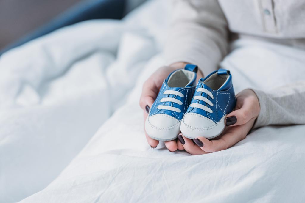 cropped view of woman holding baby shoes while lying in bed - Photo, Image