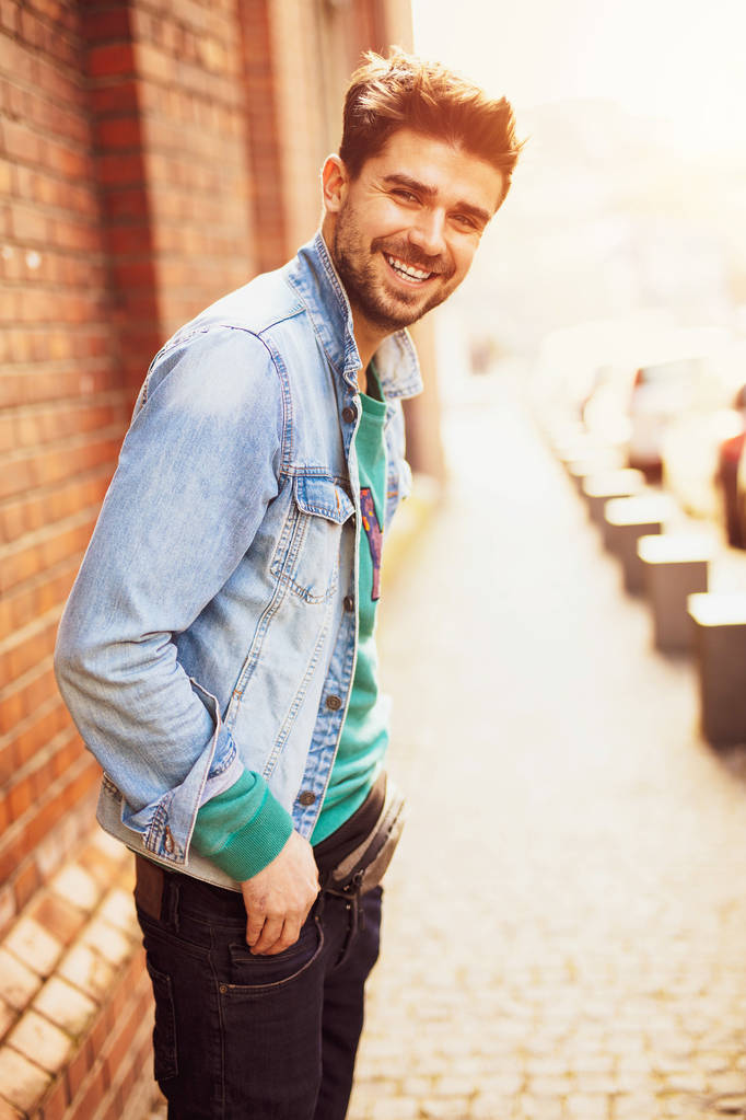 immagine di stile di vita con un uomo giovane e moderno che cammina per strada con un atittude positivo, sorridente, croce a un muro di mattoni
 - Foto, immagini